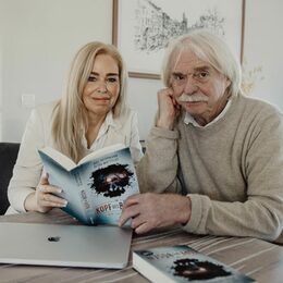 Petra Mattfeldt und Axel Petermann sitzen an einem Tisch und zeigen ihr gemeinsames Buch in die Kamera. Auf dem Tisch außerdem ein Laptop und ein weiteres Buch.