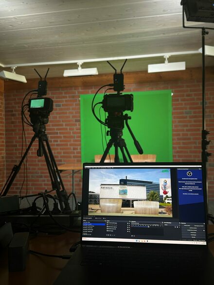 Ein Monitor und zwei Kameras stehen vor einer Leinwand.