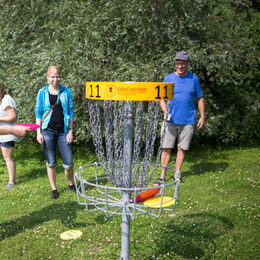 Mehrere Spieler/innen zielen auf einen Diskgolfkorb