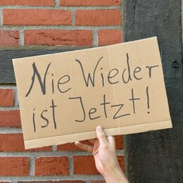 Pappschild wird von einer Hand hochgehalten. Darauf steht: Nie wieder ist jetzt!