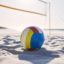 Ein Beachvolley-Ball liegt im Sand unter einem Beachvolleyball-Netz