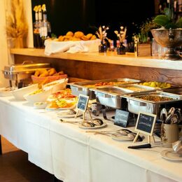 Das Bild zeigt einen Tisch auf dem ein Buffet mit kalten und heißen Speisen für ein Frühstück aufgebaut sind.