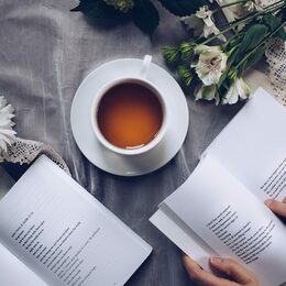 Eine Tasse mit Tee, Margariten und zwei Bücher auf einer Tischdecke.