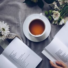 Eine Tasse mit Tee, Margariten und zwei Bücher auf einer Tischdecke.