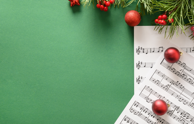 Notenblätter und rote Weihnachtskugeln vor grünem Hintergrund
